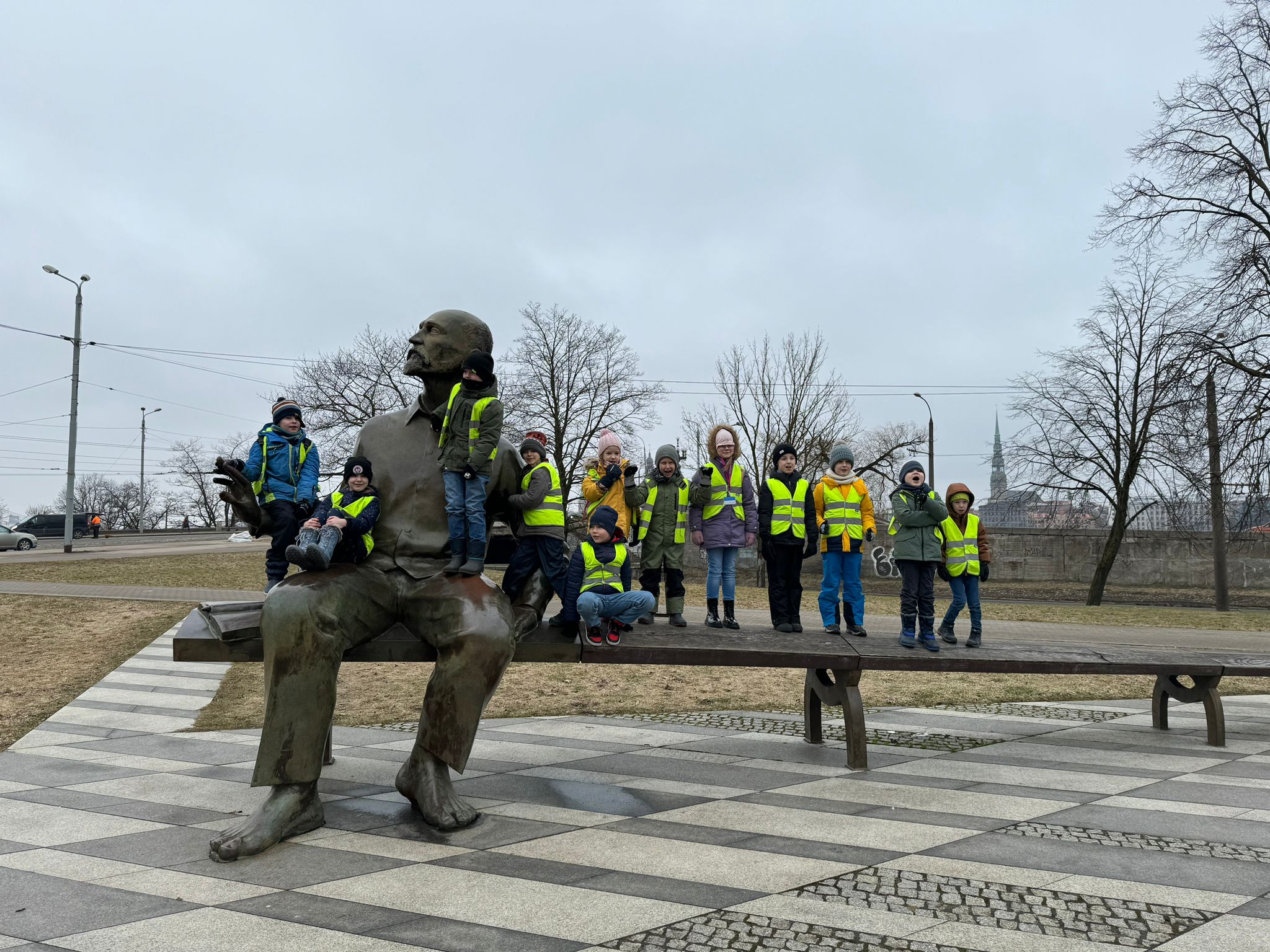 Skolēni zaļās vestēs pie Latvijas Nacionalās biblotēkas āra uz soliņa, kas simbolozē Raini. Pie Latvijas Nacionālās bibliotēkas tika atklāta skulptūra “Divi Raiņi” - sols, uz kura sēž viens liels un viens mazs Rainis.