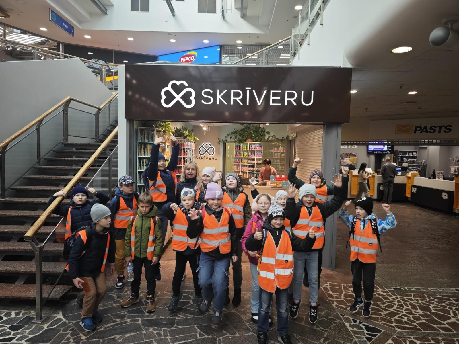 Skolēni oranžās vestēs pie Skrīveru veikala skatloga Rīgas stacijā.