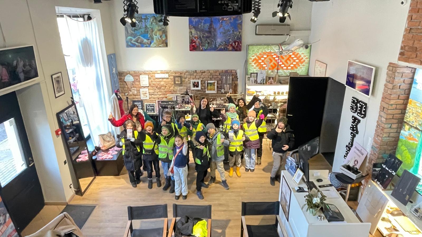 skolēni dzeltenajā vestē stāv izstāžu zāles centrā ar paceltam rokām