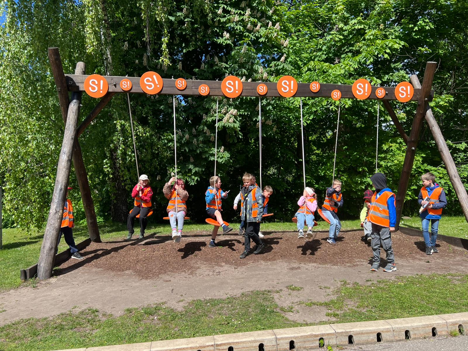 Skolēni Siguldas atrakcijā uz kopīgam šūpolēm, virsū rakstīts SIGULDA- S!