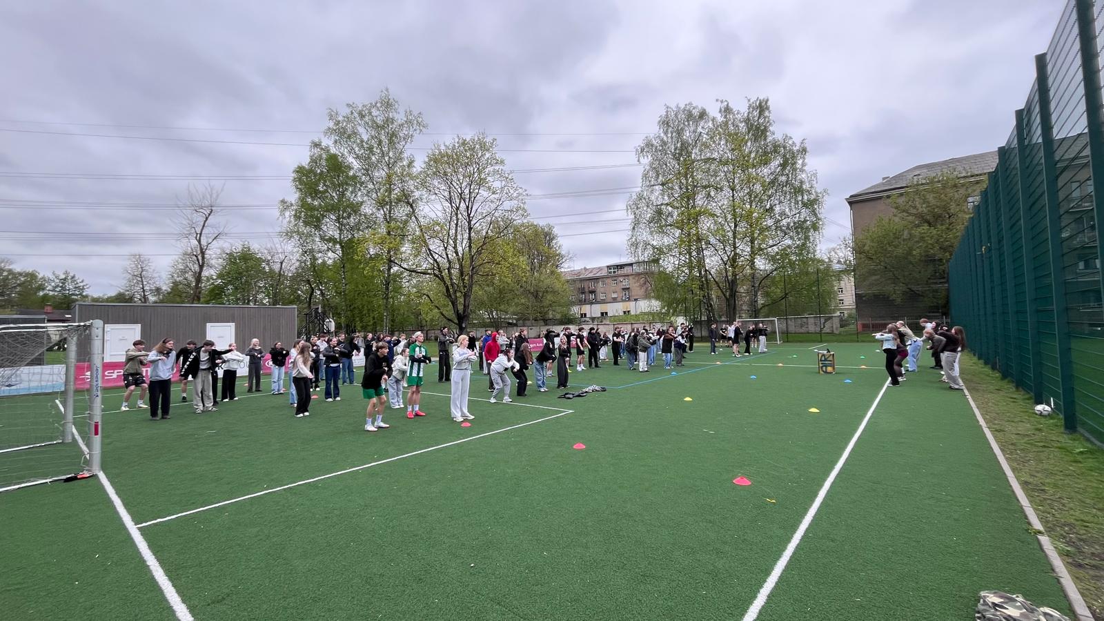 vidusskolas jaunieši skolas stadionā kopa dejo olimpisko deju